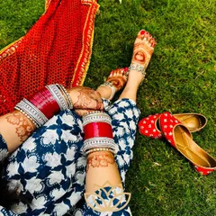 A creative shot showcasing the beautiful henna stain on both hands and feet, complemented by traditional red bangles and juttis.