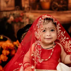 A close-up capturing the innocent and sweet expression of the baby girl in her traditional red outfit.
