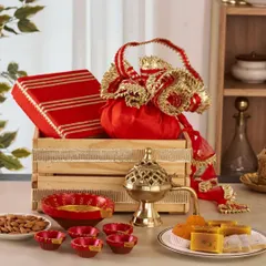 A classic Diwali gift crate, featuring a vibrant red and gold potli, a traditional brass incense burner, hand-painted diyas, and a plate of delicious Indian sweets and almonds.