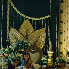 An artistic and traditional decor setup for a ceremony. We used a dark green backdrop to highlight the golden palm leaf accents, jasmine garlands, and a traditional doll, creating a rich, cultural ambiance.