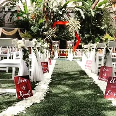 We create elegant and memorable pathways for your most special moments. This Christian wedding aisle is lined with fresh white rose petals and personalized signs, leading to a beautifully decorated altar in a lush garden setting.