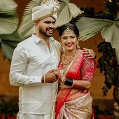 A classic portrait of a South Indian couple on their wedding day, their coordinated white and red outfits glowing with happiness.