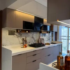 A modern L-shaped kitchen with beige handleless cabinets and a marble-patterned backsplash. This design is clean, stylish, and provides plenty of counter space for cooking.