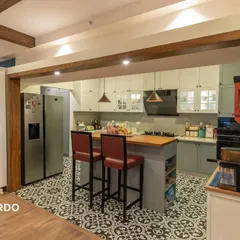 An elegant island kitchen from our Brigade Exotica project. The design features a pleasant powder grey and white color scheme, patterned floor tiles, and a large wooden island that doubles as a breakfast bar.