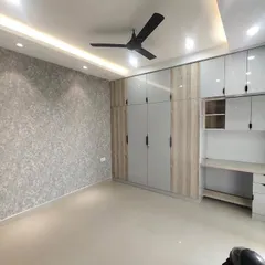 A finished bedroom with a full-wall wardrobe and an integrated study unit. The combination of grey and wood-grain laminate, along with a textured wallpaper, creates a sophisticated and functional space.