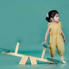A simple and modern studio portrait. The solid teal background makes the little girl in her yellow jumpsuit stand out beautifully.