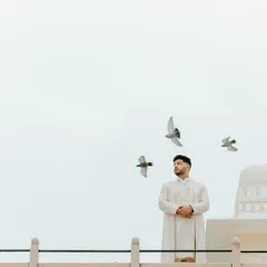 A groom stands with quiet confidence against a vast sky, with birds in flight. This artistic portrait captures a moment of reflection and poise before the ceremony begins.