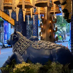 A majestic Nandi bull statue at the entrance of a Ganesh Chaturthi celebration, set under a canopy of traditional temple bells and floral strings.