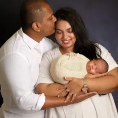 A tender moment between new parents and their baby. The father's gentle kiss on the mother's forehead shows the love and awe of this special time. This is a classic newborn family portrait.