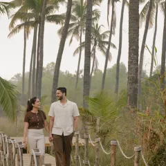 A candid shot of Vinay and Yachi walking and talking on a wooden boardwalk. Surrounded by palm trees, this image captures their easy-going chemistry and the relaxed vibe of their shoot.