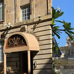 A split-screen view of Bombay House and the Flora Fountain. This composition contrasts the straight lines of colonial architecture with the soft curves of a public sculpture and nature.
