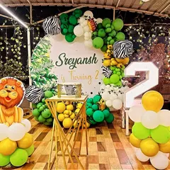 A vibrant jungle theme for a second birthday. This setup features a lion cutout on a balloon pillar, a backdrop with jungle leaves, zebra-print balloons, and a large light-up number '2'.
