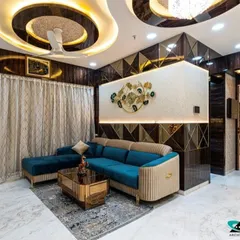 This living room in Jogeshwari is the epitome of modern luxury. We designed a complex, multi-layered ceiling with cove lighting to create drama and warmth. The combination of a plush teal sofa, reflective geometric wall panels, and bespoke furniture creates a space that is both glamorous and inviting, perfect for entertaining or relaxing.