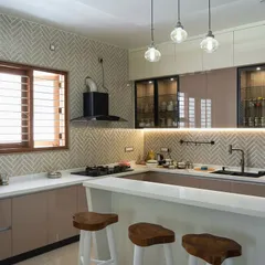 A spacious and elegant kitchen with a breakfast bar. The design features beige and glass cabinets, a herringbone backsplash, and stylish pendant lights, combining functionality with high-end aesthetics.