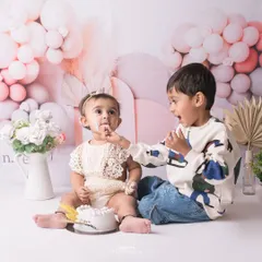 A sweet moment of sharing during a cake smash. The older brother gently gives his baby sister a taste of her first birthday cake.