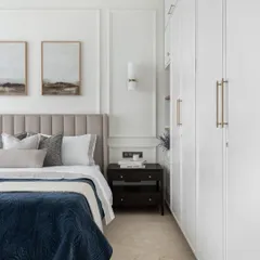 A serene bedroom setting where classic English design meets modern comfort. The wall mouldings and soft, neutral color palette create a calm atmosphere, while the plush headboard and layered bedding add a touch of luxury.