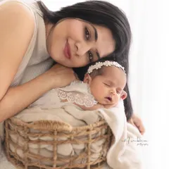 A mother's gentle love. She rests her head near her sleeping newborn, who is nestled safely in a rustic basket. A portrait of peace and deep affection.