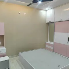A bright and cheerful bedroom designed for a younger family member, with a pink and white color palette for the wardrobe and study unit. The space is functional, organized, and personalized.