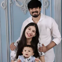 A classic family pose, with the baby sitting comfortably on his mother's lap while his father stands behind them.