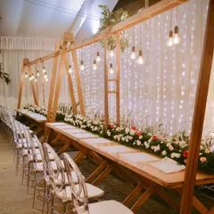 Elegant furniture can transform a space. Here, modern wooden tables are paired with transparent ghost chairs, set against a backdrop of fairy lights for a chic reception look.