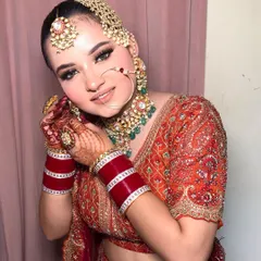 A close-up of Bhoomi's radiant bridal makeup. The look features soft shimmer on the eyes and a classic red chooda, perfectly complementing her orange and red lehenga.