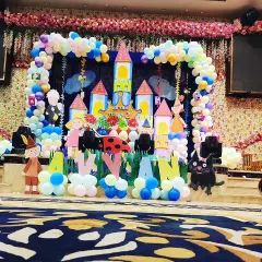 A whimsical castle theme perfect for a storybook birthday. This stage setup includes a large castle backdrop, character cutouts from a classic tale, and a balloon arch, with the birthday boy's name 'AVYAN' spelled out in front.