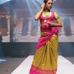 This shot from the NAVATAAR Fashion Show highlights a beautiful fusion of colors. The dramatic overhead spotlight isolates the model, drawing attention to the intricate draping of the traditional saree and her graceful pose.
