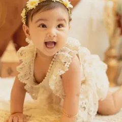 A perfect sitter session portrait. This baby girl, dressed in a lovely lace romper, shows off her crawling skills with a big, happy smile.