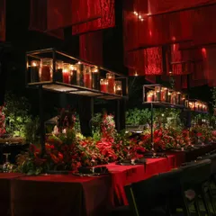 An intimate look at the dining setup for the 'Red Royal Affair'. Long tables were draped in red velvet, with overhead installations of suspended red fabric and tiered candle shelves creating a warm, romantic glow.
