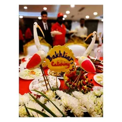 My branding is part of the presentation. This centerpiece features our "Bakhtiar's Catering" logo, surrounded by beautiful vegetable-carved birds and fresh flowers.