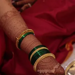 A close-up showing the deep maroon stain of the mehndi against the client's skin and her green bangles.