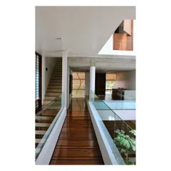 A wooden bridge traverses the central courtyard of the "Boxed In House," connecting different living spaces. This design element, crafted from recycled teak, enhances visual connectivity in a narrow urban plot.