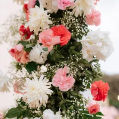 A close-up showcasing the beauty and freshness of our floral arrangements. This pillar is adorned with a mix of pink and red carnations, white chrysanthemums, and delicate baby's breath.