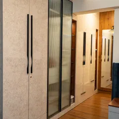 This wardrobe holds a clever secret. The design features a mix of textured laminate and fluted glass doors, with a small, custom-sized pouf tucked neatly into its own niche, ready to be pulled out for a comfortable seat.