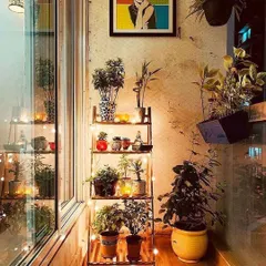 This narrow balcony space is maximized with a ladder-style plant stand, allowing for a vertical display of various plants. String lights and a pop-art print on the wall add personality and warmth.