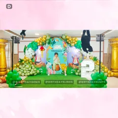 A wide view of the complete jungle stage setup for a second birthday, featuring a personalized backdrop and a variety of animal props. The green astroturf and balloon garlands in green and gold create a vibrant, cohesive look.