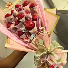 Two hands hold this lovely pink-wrapped strawberry bouquet, showing its generous size. It's a gift meant to be shared, or enjoyed all by yourself.