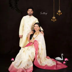 A regal couple portrait celebrating their journey together. The classic off-white and pink saree, paired with traditional jewelry and elegant studio props, creates a timeless and sophisticated memory.
