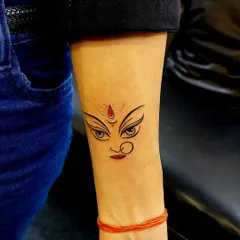 The powerful eyes of the Goddess Durga, captured in a minimalist design. With a simple red bindi for contrast, this tattoo is a subtle yet strong symbol of divine feminine power.