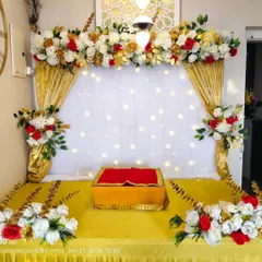 This is the same classic gold drape and floral setup, shown with a different lighting angle. The overhead light highlights the intricate floral arrangement on top, featuring red, white, and golden flowers.