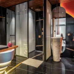 This bathroom combines dark, dramatic elements with vibrant color. We used black marble flooring and walls, contrasted with a striking, backlit orange alabaster panel and a freestanding tub to create a unique, high-energy space.