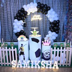 A football-themed birthday party setup with a black and white balloon ring. The pedestals are customized with football graphics, and the name is displayed in bright marquee letters.