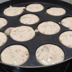 The batter for puddu being poured into the pan. You can see the mix of herbs and vegetables in the batter before cooking.