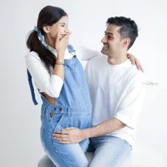 Capturing a moment of pure, unscripted joy. This candid shot of a couple sharing a laugh in casual denim overalls shows that maternity photos can be fun and feel just like you.