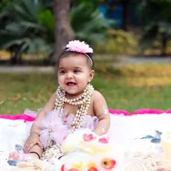 A huge, happy smile from a baby girl during her outdoor cake smash session. The natural light and pink balloons create a beautiful, celebratory atmosphere.