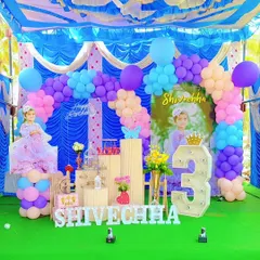 A vibrant outdoor birthday celebration under a tent. The colorful balloon arch and custom backdrop create a festive atmosphere for a third birthday party.