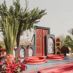 The 'Gulmohar Bagh' Haldi setup, featuring bold red decor elements and traditional seating against a stunning backdrop of the Udaipur hills.