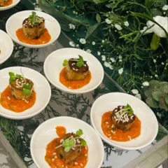 An artfully presented appetizer featuring a savory base with a rich topping, garnished with microgreens. This bite is served on an individual white dish, showcasing our attention to detail in plating and presentation.