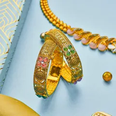 A close-up from the PNGadgil campaign, focusing on these intricately designed gold bangles. The soft blue background makes the warm gold and colorful enamel work really pop.