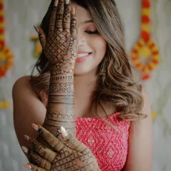A classic mehndi pose. The bride shows off her detailed henna, which extends up her arm, while her happy smile peeks out from behind her hand.